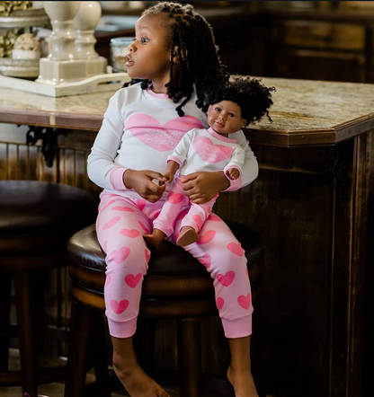 Young girl wearing matching pajamas with her 18 inch doll, featuring pink heart print and positive affirmation sleepwear set